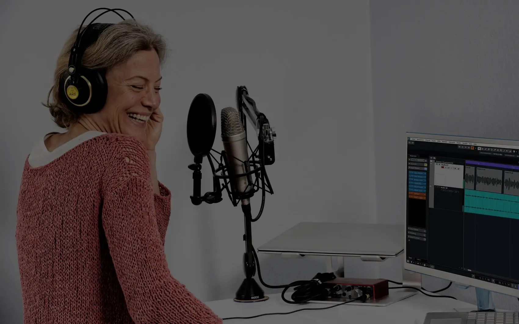 Pirjo Katinka Arregger lacht im Home Studio vor dem Mikrofon, am Bildschirm die Aufnahmespur